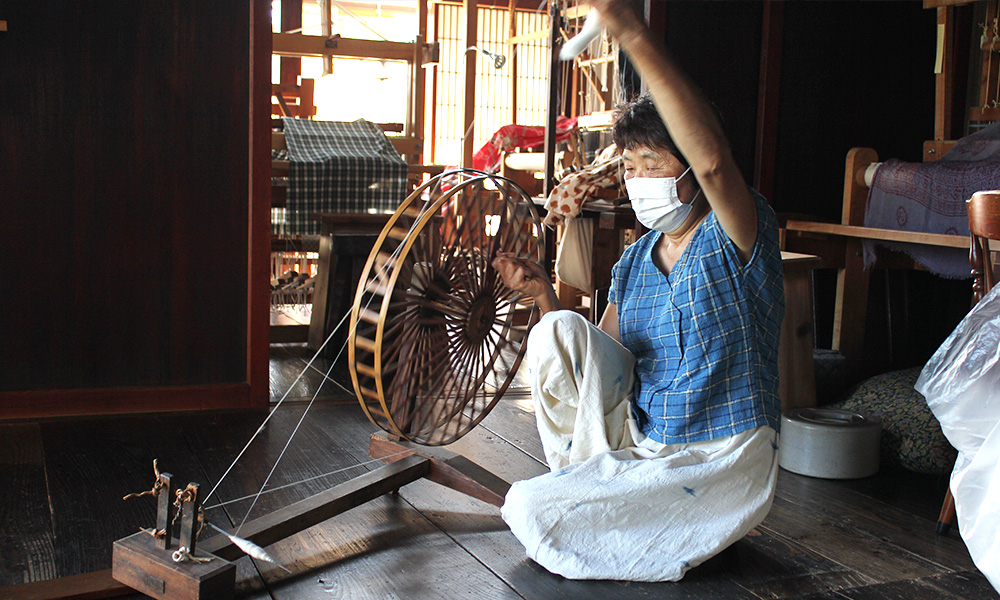 糸車を使って、スルスルと糸を紡いでいく豊子さん。手に持っているのが、打ちほぐされた綿を丸めた「よりこ」と呼ばれる綿の固まり。